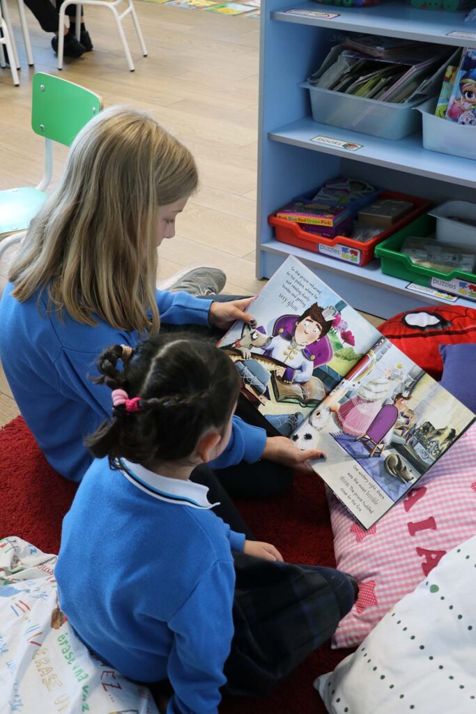 Estudiante de primaria Casvi leyendo un libro a una estudiante de infantil. Beneficios de leer libros todos los días