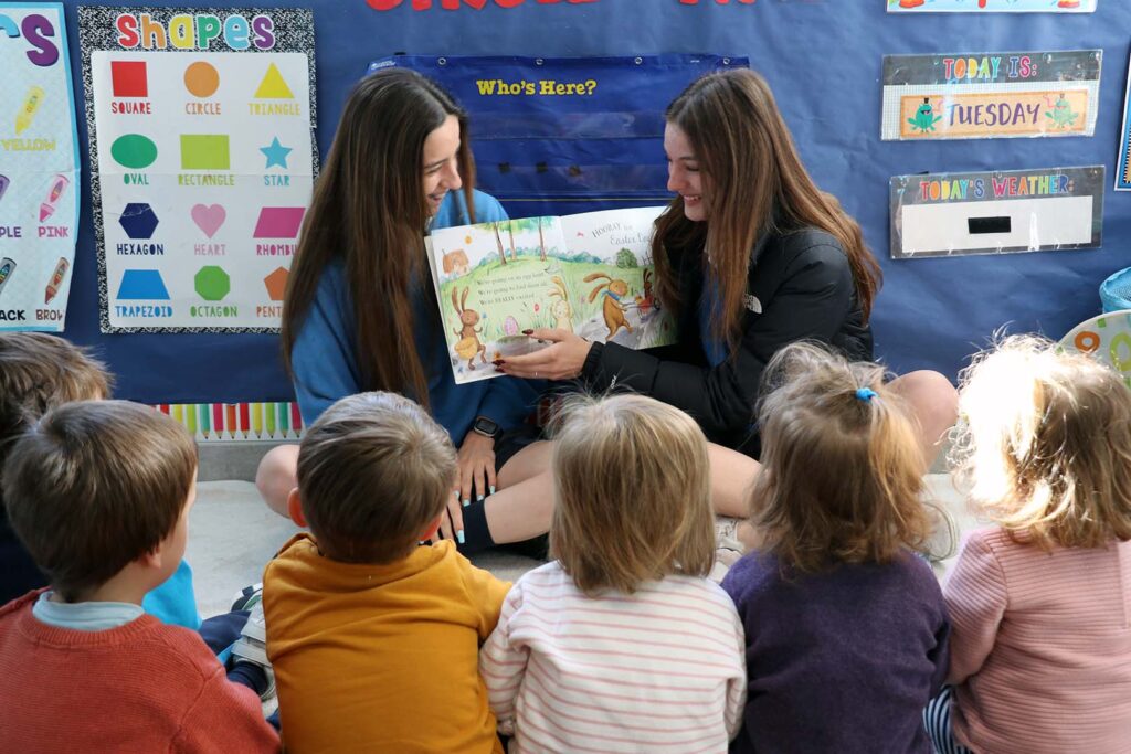 Dos alumnas de Cavsi International American School leyendo un cuento a niños de guardería