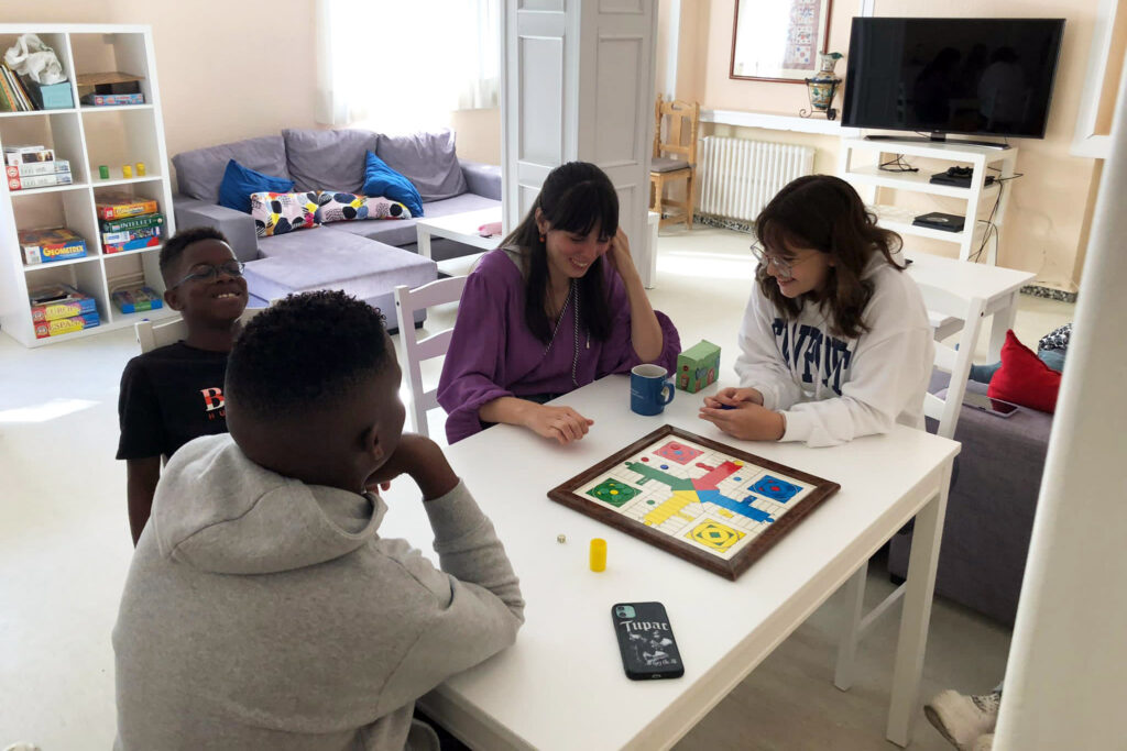 Niños residentes y educadores jugando a un juego de mesa en el salón de la residencia de estudiantes de Casvi International American School. Internados en España
