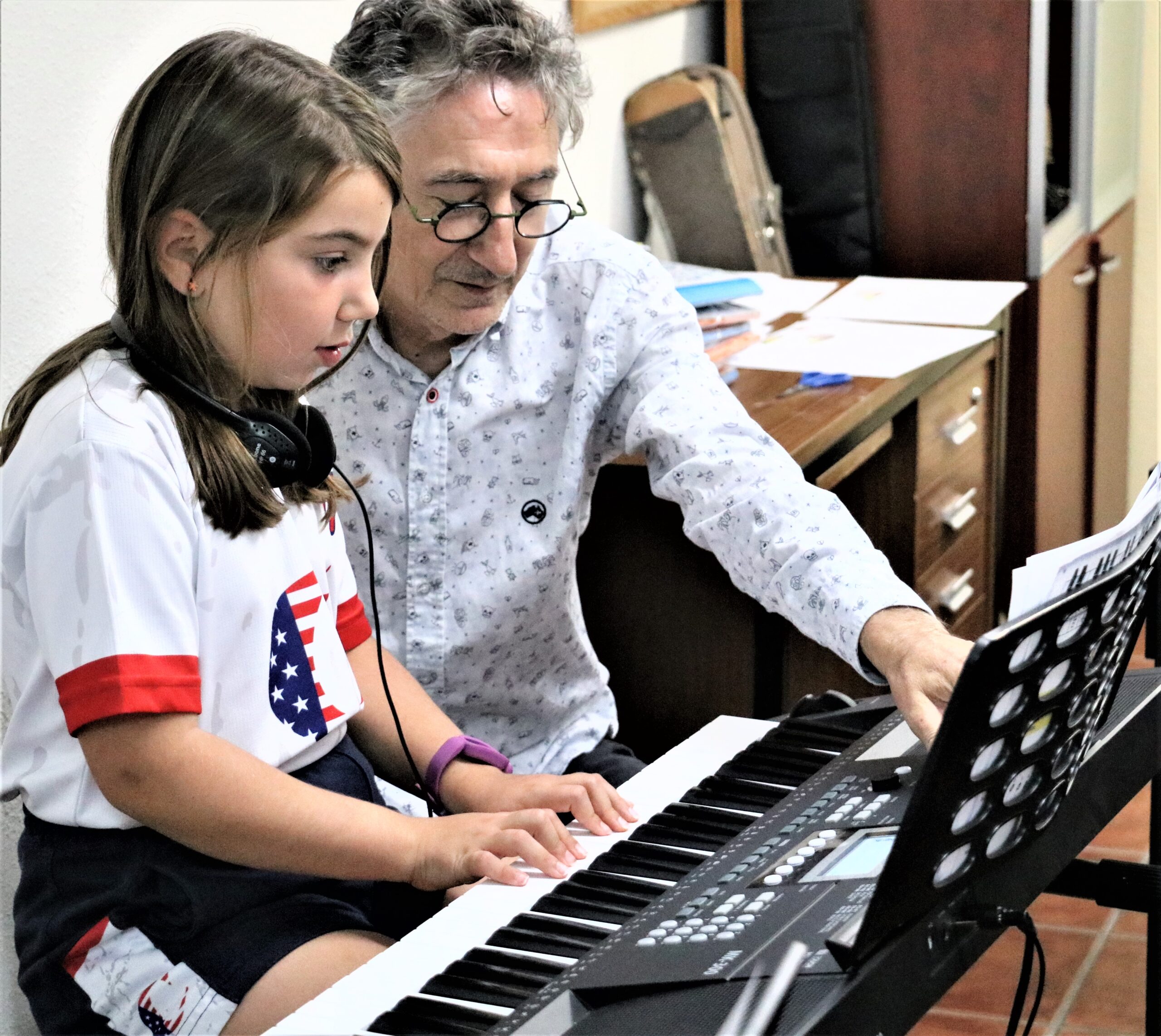 Un niño toca el piano con disciplina y concentración, recibiendo la guía paciente y respetuosa de su profesor durante la clase de música.